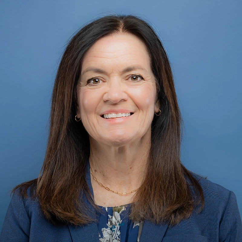 Michele Busse smiles into the camera against a blue background.