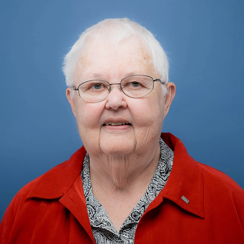Sister Margaret Weigel smiles into the camera against a blue background.