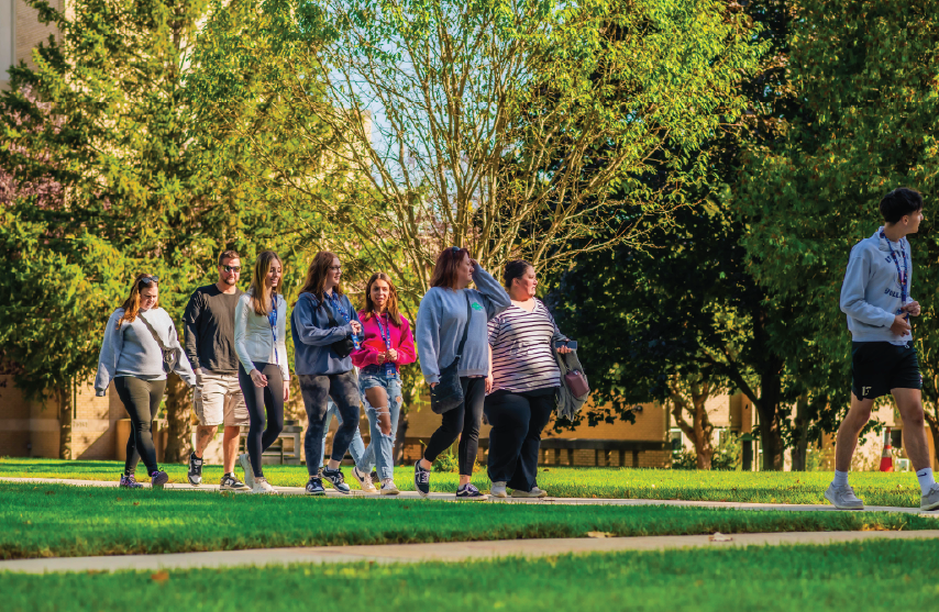 Large group of students on a campus tour surrounded by trees