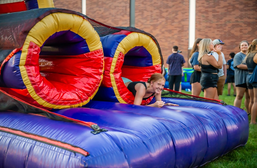 A girl crawls out of a colorful obstacle course.