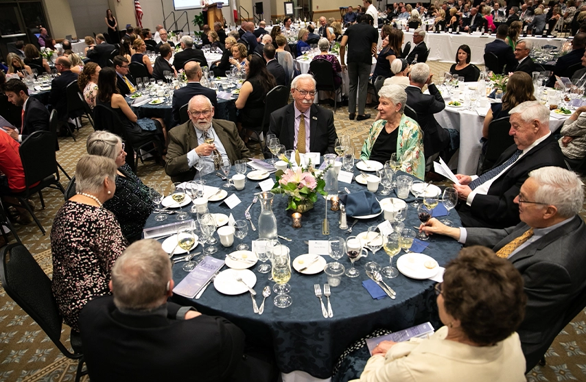 A group of well-dressed alumni chat at a circular dining table.