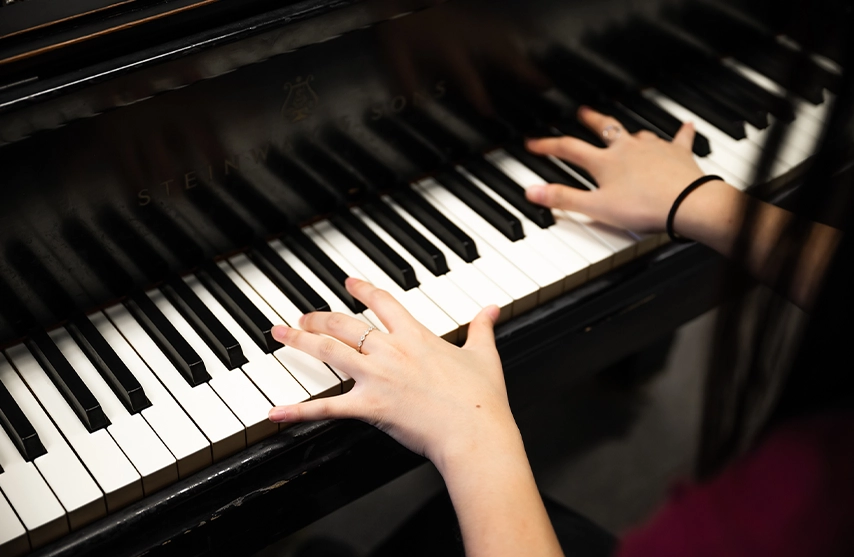 A close-up of a woman playing the keys of a black piano.