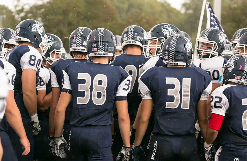 A group of football players huddle, dressed in their uniforms