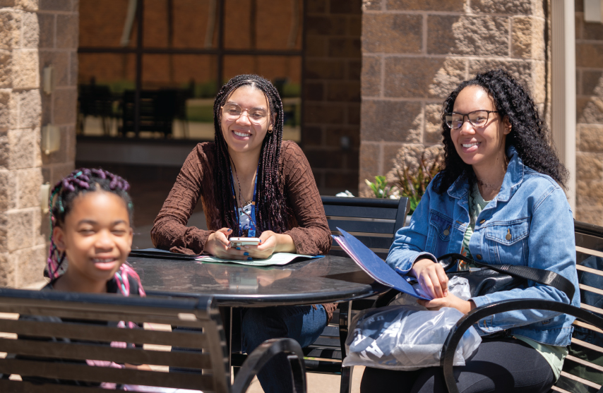 2 students and a child sitting together at a table outside