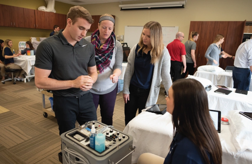 Physical therapy students discussing techniques in a lab setting.