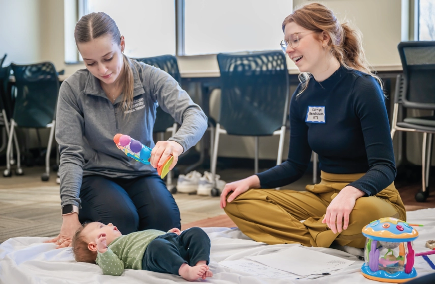 Physical therapist assesses young patient in pediatrics lab with parent nearby.