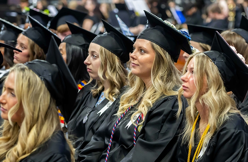Graduates in caps and gowns seated at a commencement ceremony.