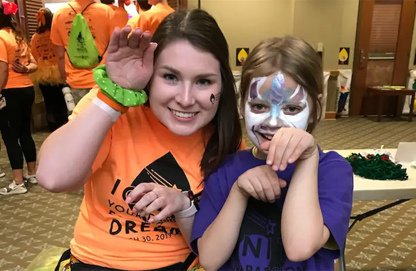 A smiling woman posing with a child with a painted face.