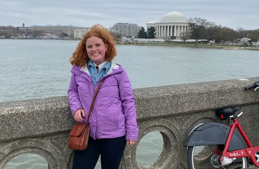 A student posing for a picture outside by a lake.