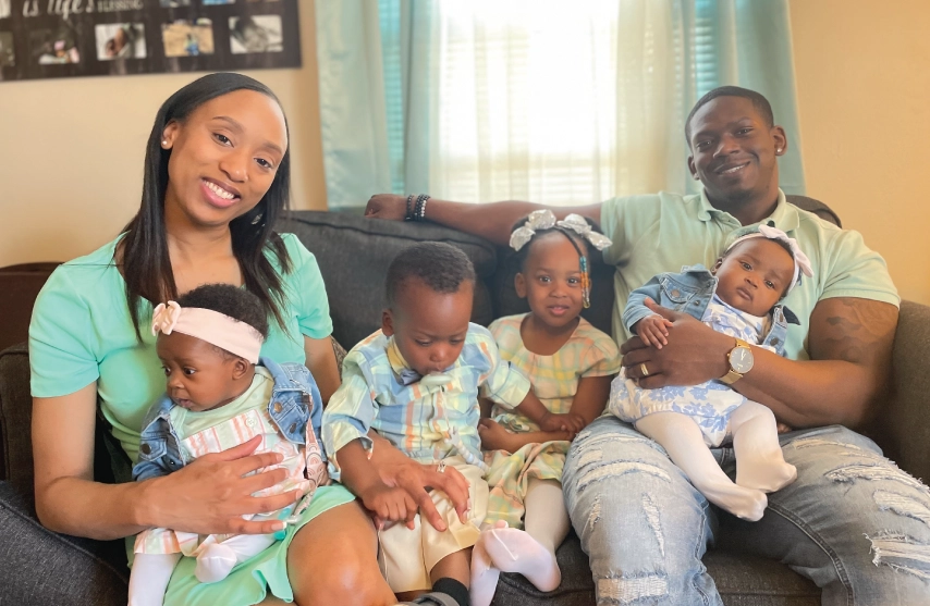 A man and a Woman sitting on a couch with 4 young children.