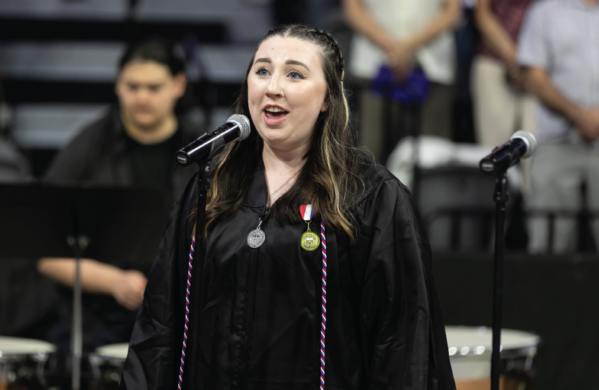 Student in graduation gown singing at commencement event.