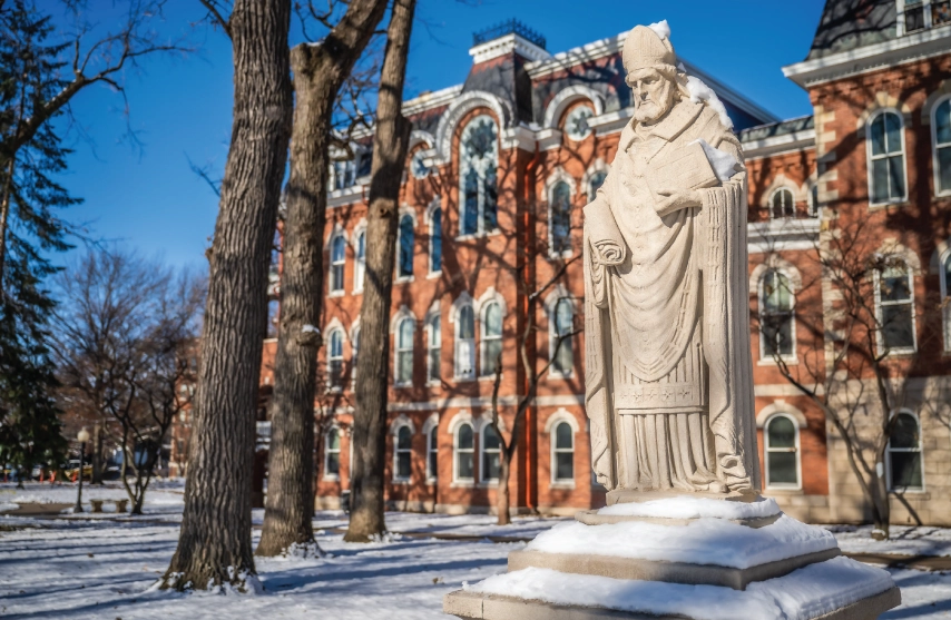 A stone statue of Saint Ambrose of Milan outside in the snow.