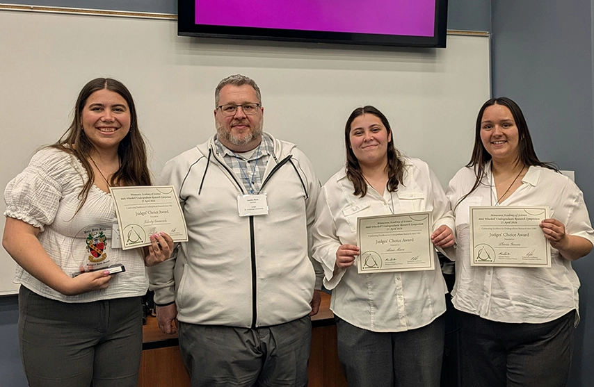 Left to right: Felicity Emmerich, Associate Professor Justin Rice, Alina Maca, and Lluvia Garcia pose for a photo at the Minnesota Academy of Science 2026 Winchell Symposium Awards ceremony, with students holding award certificates.