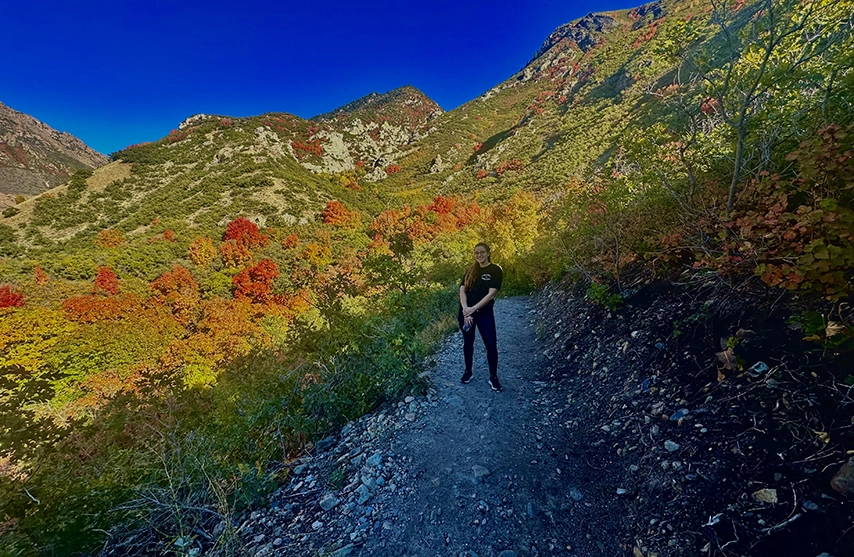 Cristina Lugo stands on a dirt path surrounded by yellow and red trees.