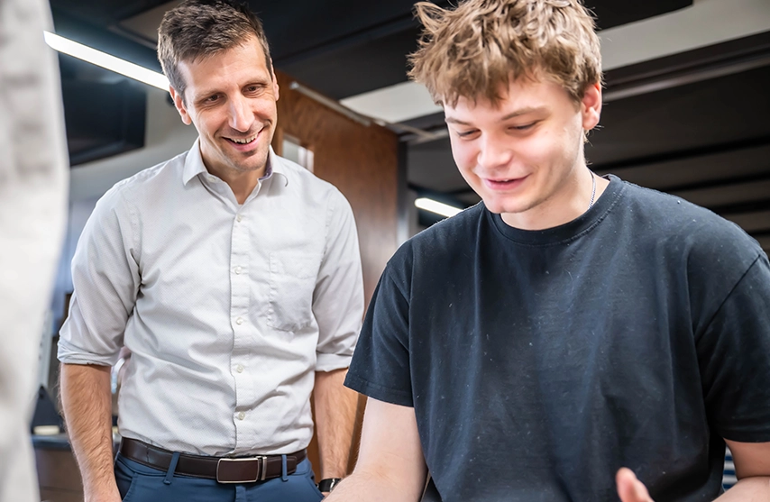 A students smiles down at his work as he works with his instructor during an engineering lab at St. Ambrose University.