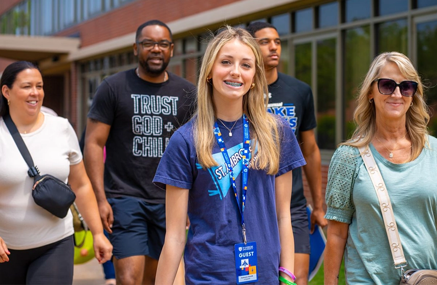 A small group of people tour St. Ambrose University, some smile into the camera.