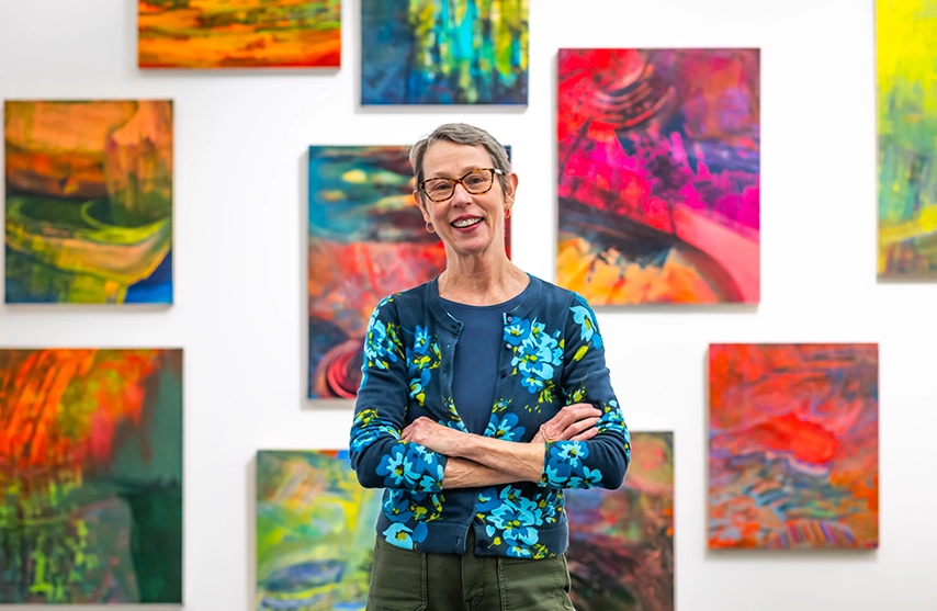 Kristin Quinn, MFA, stands in front of her “Luminous Flux Paintings from the Watershed” art collection on display at the Figge Art Museum,