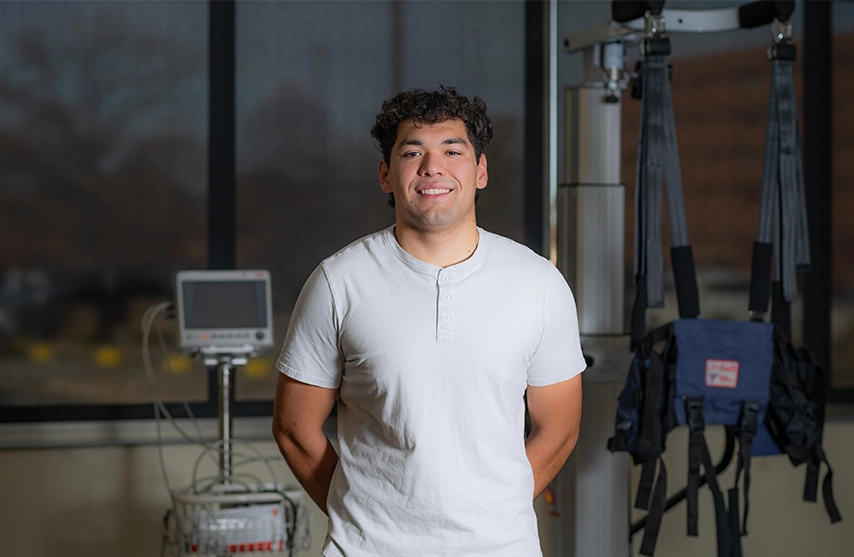Oscar Mejia, '27 DPT, stands in an physical therapy lab at St. Ambrose University and smiles into the camera.