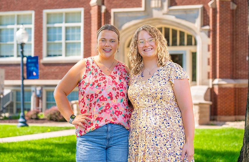 Grace Bickle and Megan McConnaughay stand next to each other and smile at the camera.