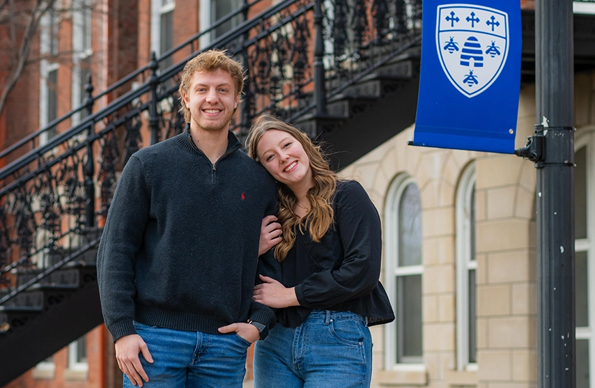 Jaxson Eisenbarth ‘27 walked Ellie Seberger ‘26 stand together and smile at the camera on the St. Ambrose University campus.