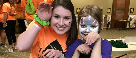 A smiling woman posing with a child with a painted face