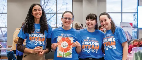 Four students smiling together wearing blue shirts that say 