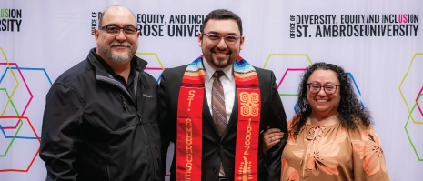 A student with a cultural stole posing with parental figures.