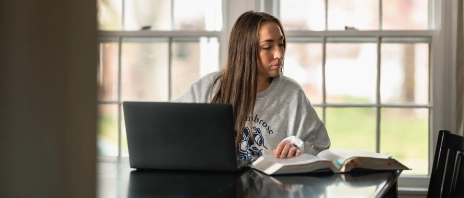 student at laptop, glancing aside at notes