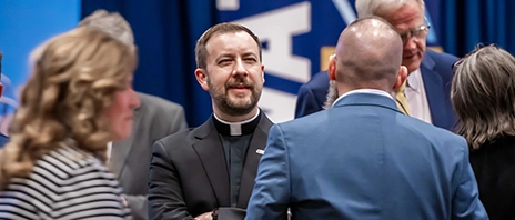 Father Thomas J. Hennen, '00, faces the camera as he talks with fellow alumni who face away from the camera.