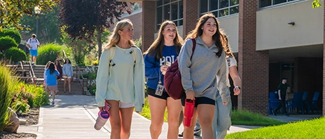 Three SAU students walking on campus smiling with backpacks on