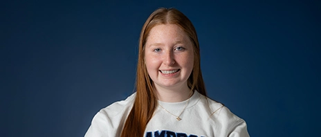 Jillian Aslip, '29, sits at a table and smiles into the camera.
