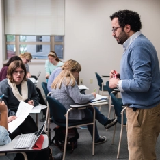 A man standing in front of a classroom full of students, giving a lecture.