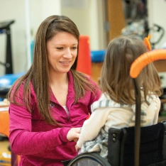 A woman working with a child in a wheelchair to overcome challenges.