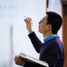 A professor writing on a whiteboard in a math course.