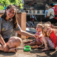 A women sitting with two young children, smiling and playing together outdoors.