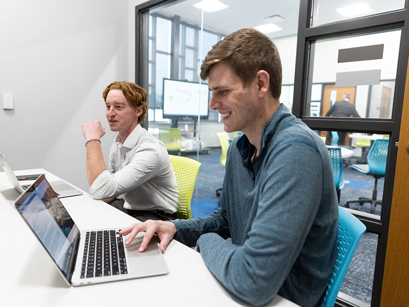 Two business major students work from their laptops.