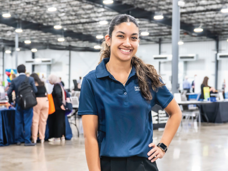 A student standing in center of career fair, smiling.