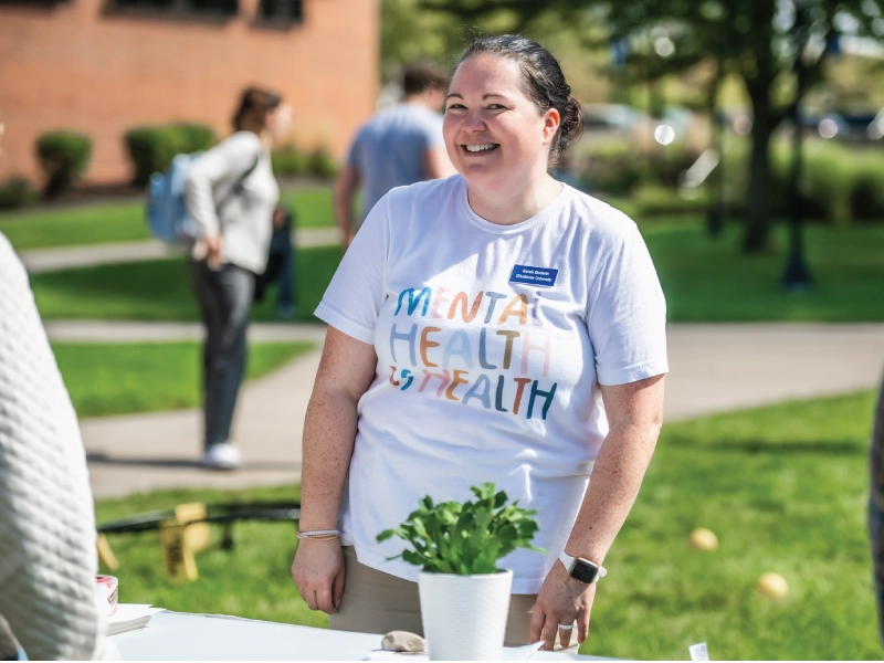 Woman at booth wearing mental health advocacy shirt.