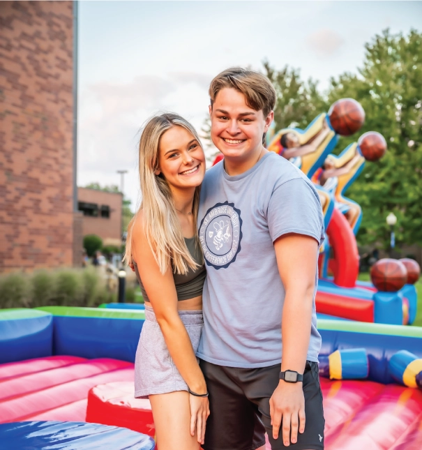 Two students smiling at an outdoor event standing on a bouncy platform.