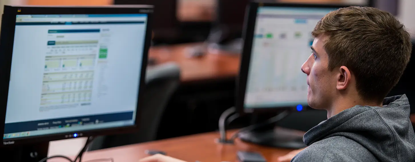 A male student sitting at a desk in front of a computer screen.