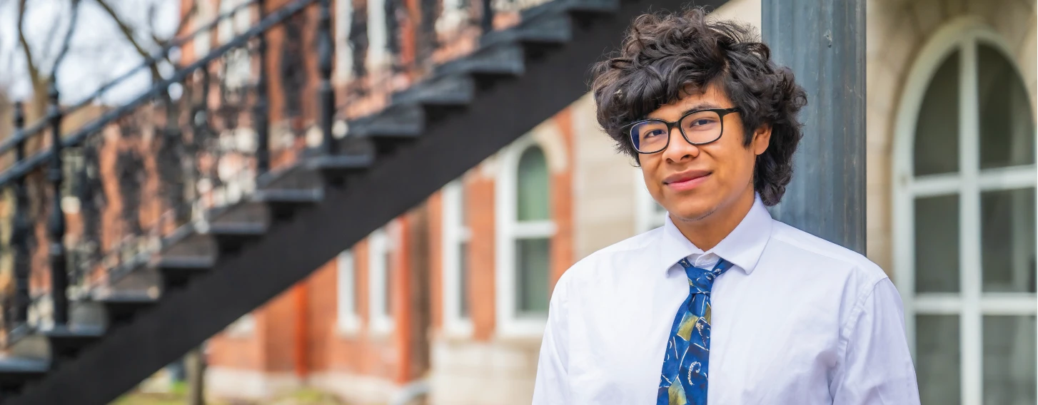 Student stands outdoors in front of brick building.