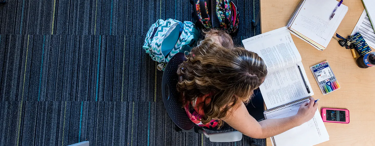 Two students sitting at a table, taking notes and reading textbooks.