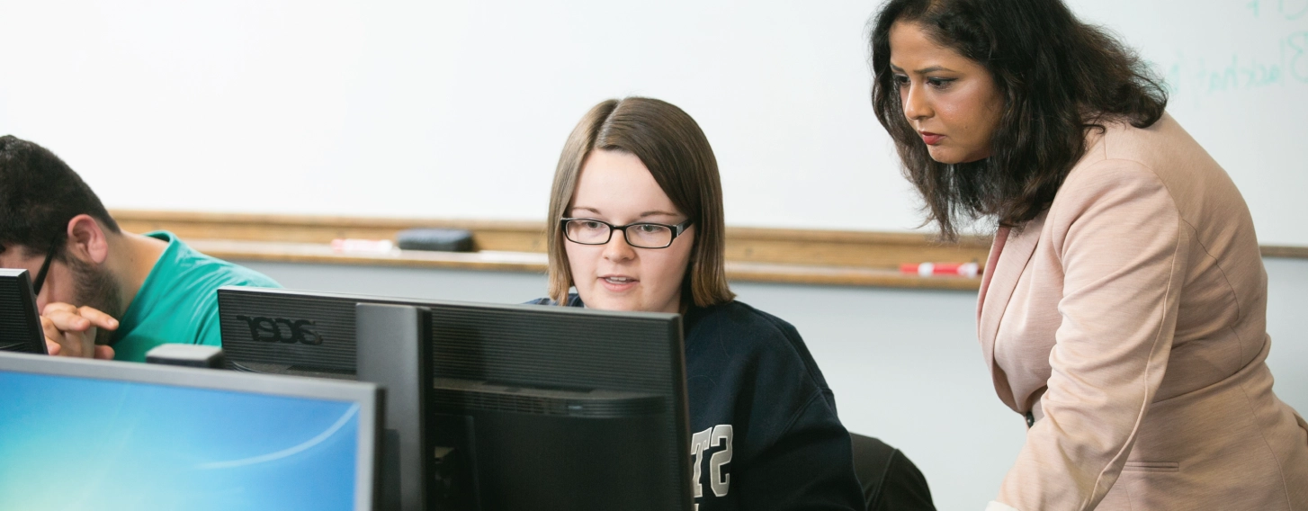 A woman helping a student on a computer in a classroom.