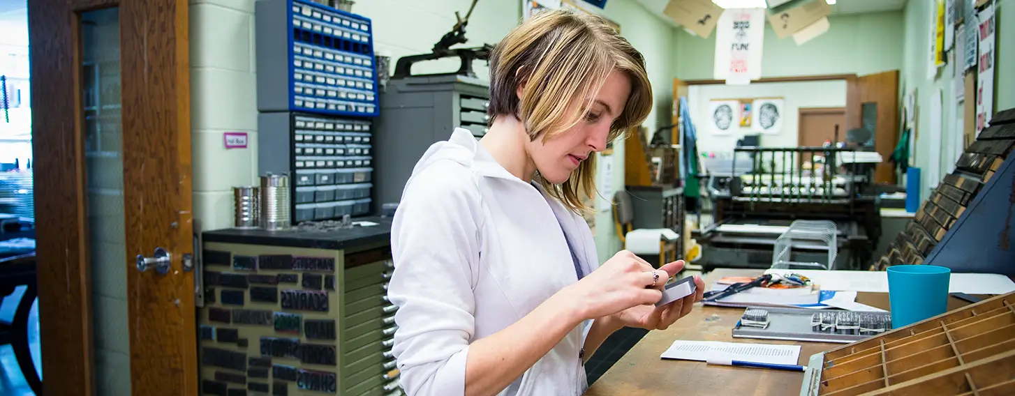 A woman working with a letterpress at a wooden work table.