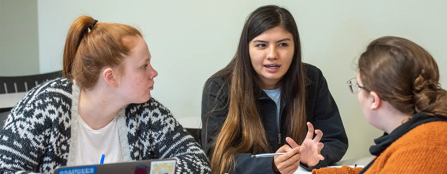 Three students engaged in a lively conversation while sitting at a table.