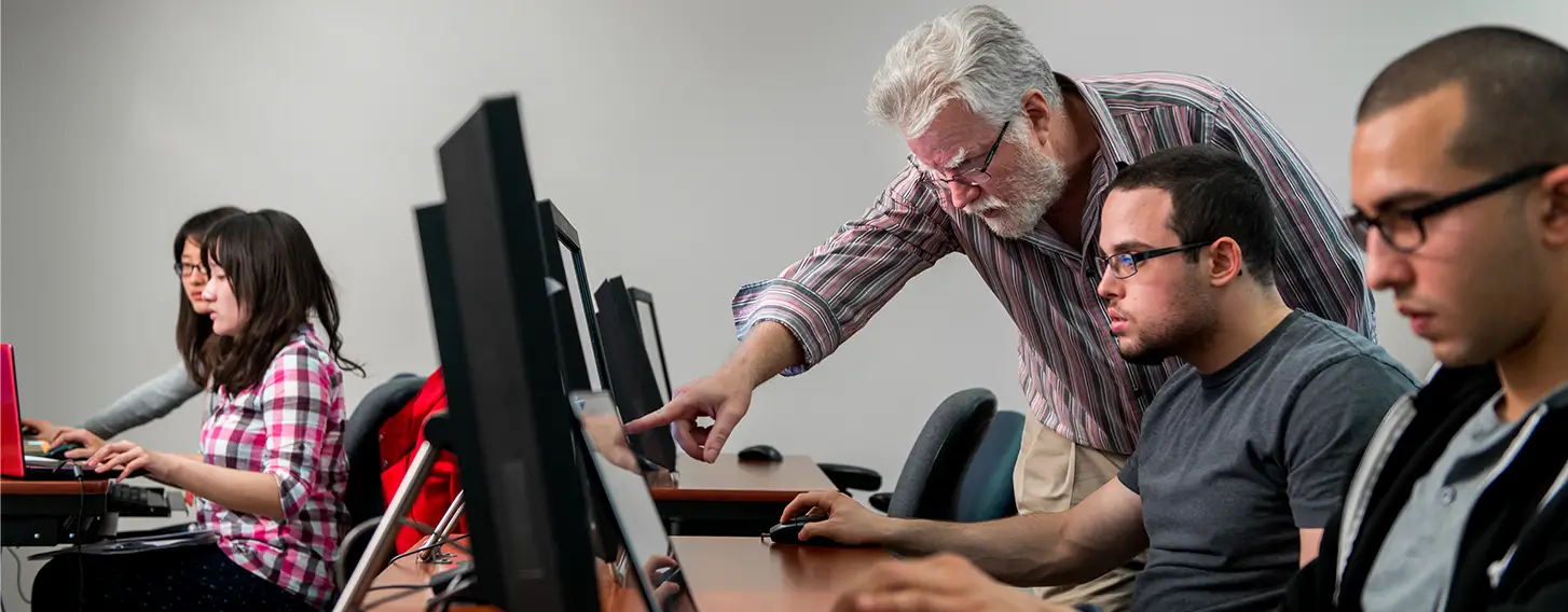 A man instructing students who are using computers in a classroom setting.