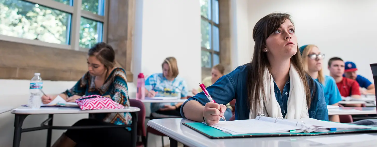 Students taking notes sitting at desks in a classroom setting.