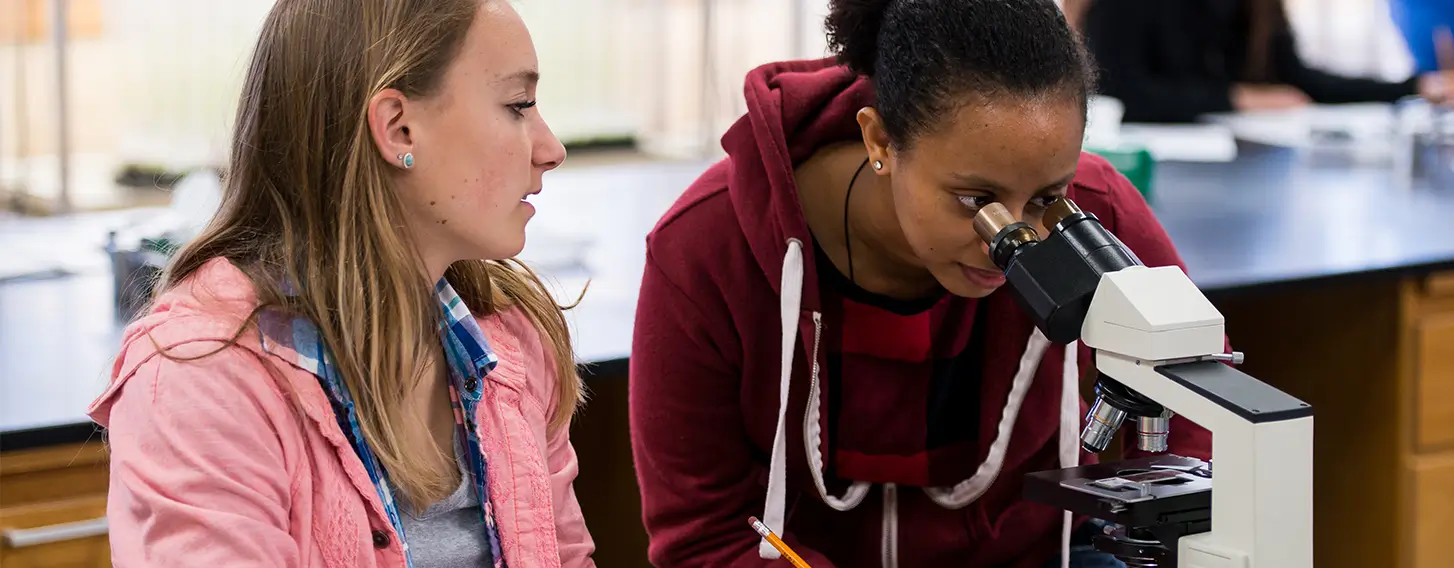 Two students observing through a microscope in a biology lab.