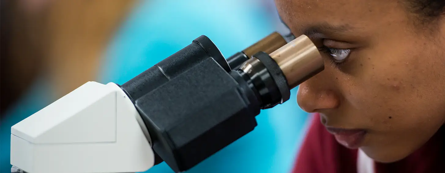 A woman examining a specimen under a microscope.