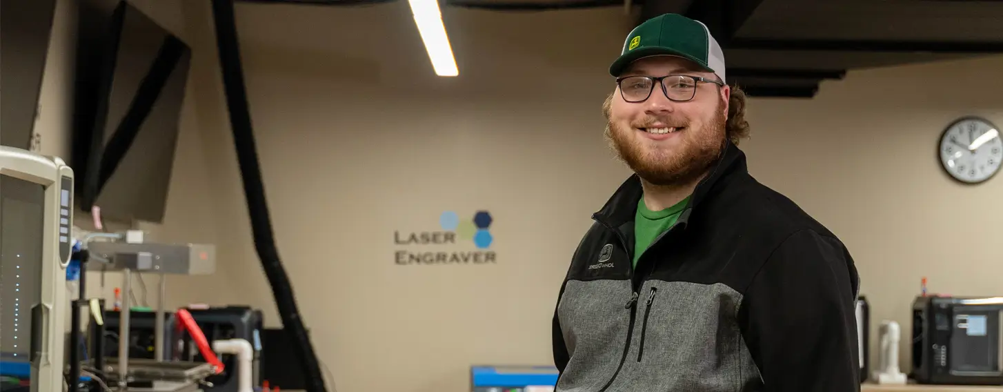 An engineering student posing for a portrait in a lab near a laser engraver.